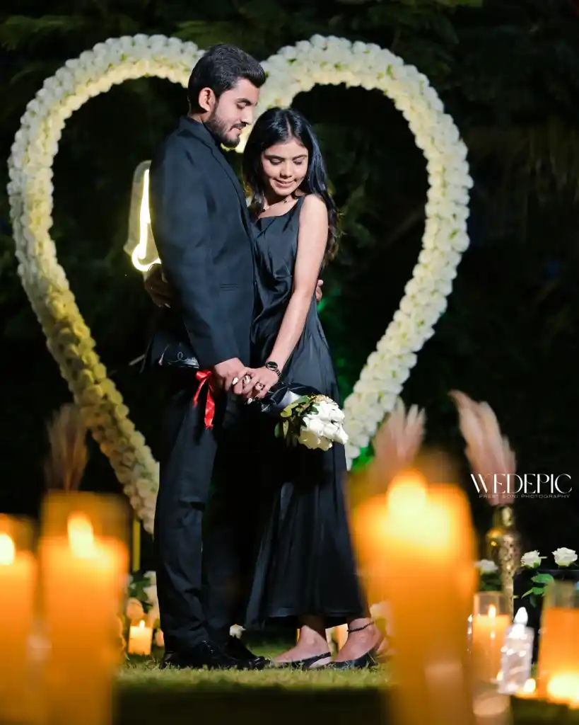 Couple in black holding a bouquet inside a floral heart lit by candles