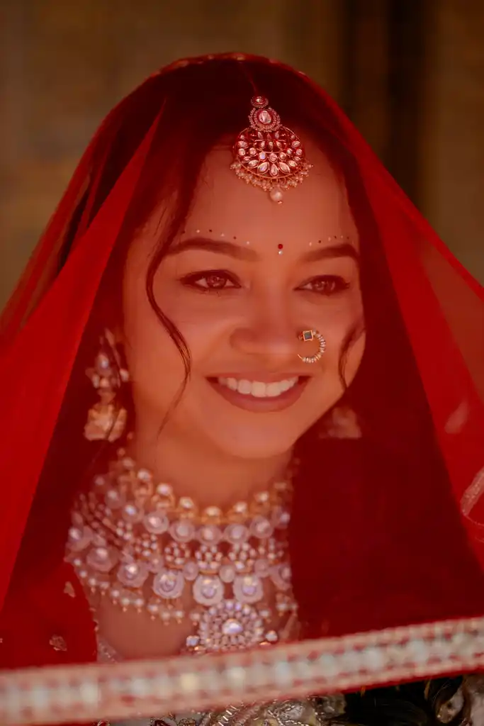 Bride smiling beneath a red veil in kundan jewellery