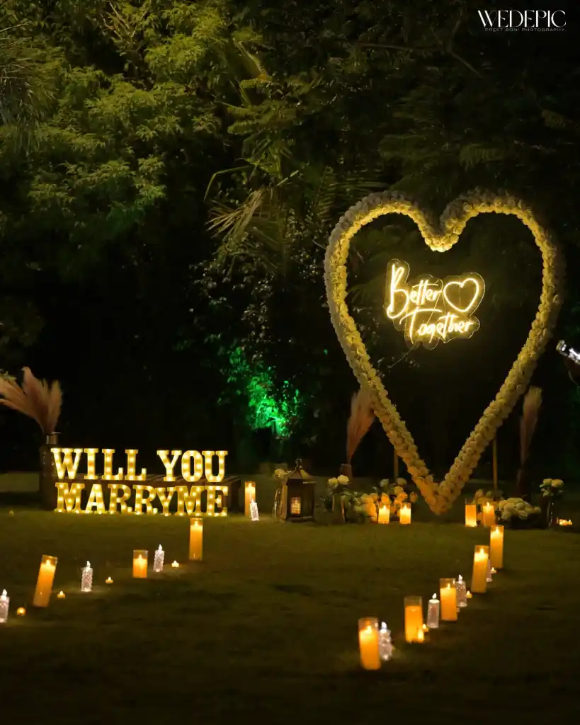 Candlelit Will You Marry Me proposal setup with a floral heart arch